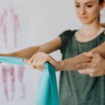 Fizjoterapeuta uczy młodą kobietę ćwiczeń z taśmą oporową w gabinecie