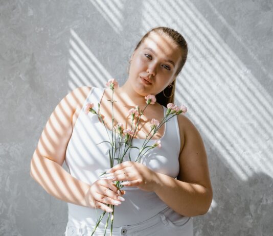 Styl sportowo‑elegancki w rozmiarze plus size: przepisy na look do miasta i do biura Kobieta plus size w topie na ramiączkach z kwiatami w świetle żaluzji