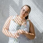 Kobieta plus size w topie trzyma kwiaty w świetle wpadającym przez żaluzje