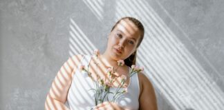Jak stylowo ubierać się plus size na randkę, by wyglądać sensualnie, a nie przebraniowo Plus size kobieta w topie trzyma bukiet kwiatów w świetle padającym z żaluzji