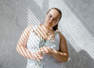 Plus size kobieta w topie trzyma bukiet kwiatów w świetle padającym z żaluzji