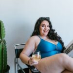 Pewna siebie kobieta plus size w stroju kąpielowym z winem i książką obok kaktus