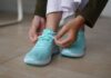 Modne buty na szeroką stopę i wysokie podbicie: jakich fasonów szukać na co dzień? Osoba wiążąca turkusowe sneakersy na drewnianej podłodze