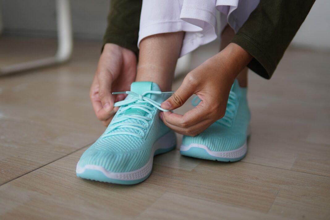 Osoba wiążąca turkusowe sneakersy na drewnianej podłodze Osoba wiążąca turkusowe sneakersy na drewnianej podłodze