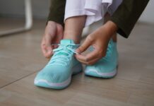 Modne buty na szeroką stopę i wysokie podbicie: jakich fasonów szukać na co dzień? Osoba wiążąca turkusowe sneakersy na drewnianej podłodze