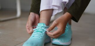 Modne buty na szeroką stopę i wysokie podbicie: jakich fasonów szukać na co dzień? Osoba wiążąca turkusowe sneakersy na drewnianej podłodze