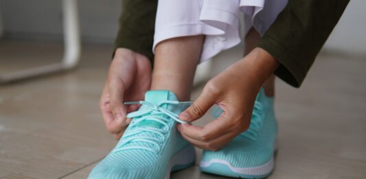 Osoba wiążąca turkusowe sneakersy na drewnianej podłodze