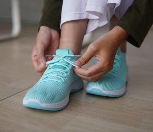 Modne buty na szeroką stopę i wysokie podbicie: jakich fasonów szukać na co dzień? Osoba wiążąca turkusowe sneakersy na drewnianej podłodze