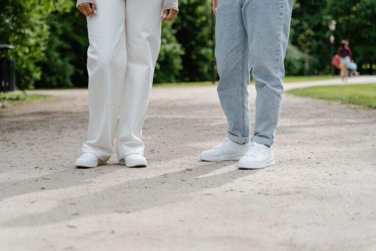 Osoby w białych sneakersach spacerujące po zielonym parku